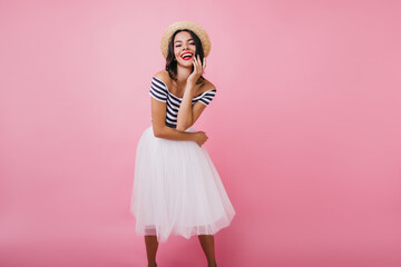 European girl wears white skirt posing with inspired smile. Latin glamorous woman in hat dancing on...