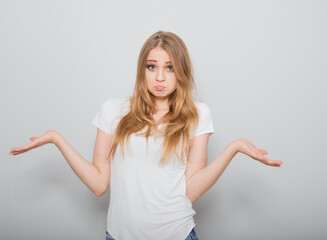 Fototapeta premium Confusion very offended fair blond hair woman thinking, looking sad and spreading her hands. Casual neutral shirt clothing on grey studio wall for isolation portrait.