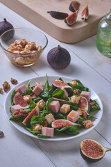 The process of making salad with figs. Ready salad and ingredients on a white wooden table.