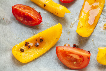 Slices of yellow bell pepper and red tomato prepared for baking with spices, close up