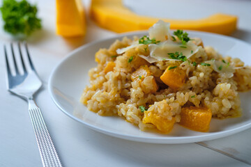 Pumpkin risotto garnished with fresh parsley and parmesan. Italian dish on a white table.