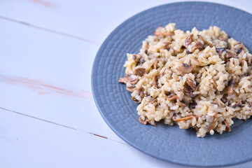 Risotto with mushrooms close-up on a gray plate. Italian dish on a white wooden table.