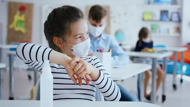 Small girl with face mask at school after covid-19 lockdown, disinfecting hands.