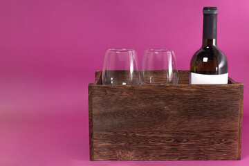 a bottle of wine and two glasses in a wooden box on a pink background