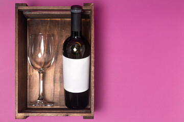 a bottle of wine and a glass in a wooden box on a pink background
