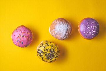 Donuts with colored icing on a yellow paper background.