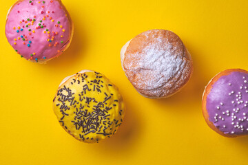 Donuts with colored icing on a yellow paper background.