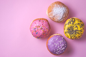 Four donuts with colored glaze on a pink paper background.