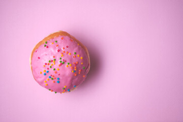 Close-up of a donut with colored glaze on a pink paper background. Top view.