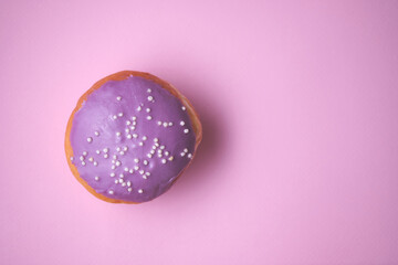 Close-up of a donut with colored glaze on a pink paper background. Top view.