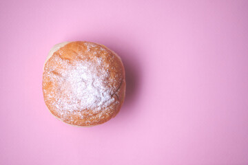 Donut decorated with icing sugar on a pink paper background close-up. View from above.