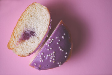 Close-up of a sliced stuffed donut decorated with colored glaze on a pink paper background. Top view.
