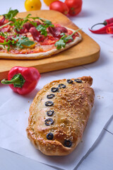 Homemade Italian pizzas: calzone with mazarella, tomatoes, tomato sauce, sausage, olives and arugula; spicy with chili pepper and smoked sausage. Italian dish on the board before serving.