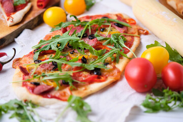 Homemade Italian spicy pizza with olives, two kinds of sausage, mazarella, tomatoes, tomato sauce, sausage, arugula, oregano and olive oil. Italian dish before serving.
