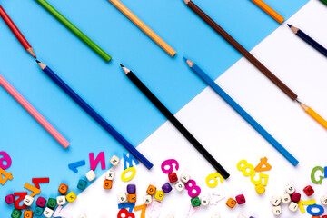 Many colorful drawing pencils and small letters on blue and white copy space background.