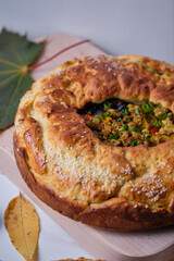 Homemade autumn pie with meat, onions and bell pepper on the board. Dish on a white wooden table. Close-up.
