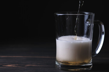 Beer is poured into a beer glass. Wooden table and black background.