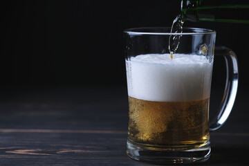 A man pours beer from a bottle into a beer glass. Wooden table and black background.