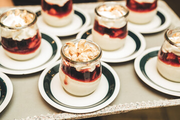 Rows of glasses with white-red sweet dessert decorated on top with cashew nuts. Self-serving buffet table. Celebration, party, birthday or wedding