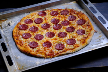 Classic pepperoni pizza with tomato sauce, cheese and salami sausage on a black wooden background.