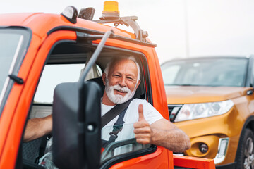 Handsome senior man working in towing service on the road and showing thumb up. Roadside assistance...