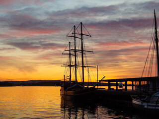 Fototapeta premium Dark ship in evening harbour. Beautiful sky with red clouds. Golden water reflections. Oslo, Norway.