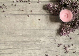 Pink candle with lilac flowers on wooden surface shot from above. Top view, flat lay, copy space. ...