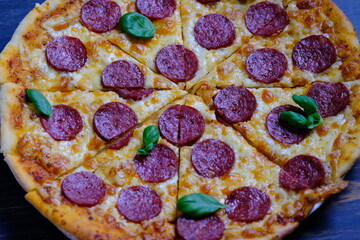 Classic pepperoni pizza with tomato sauce, cheese and salami sausage on a black wooden background.