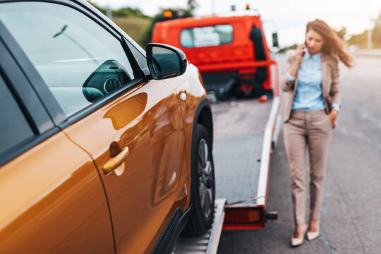 Elegant middle age business woman calling someone while towing service helping her on the road. Roadside assistance concept.