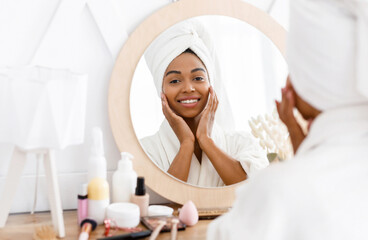 Beauty skincare. Young beautiful black woman touching her face near mirror