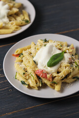 Two portions of pasta with tomatoes, spinach, parmesan and bolognese sauce. Serving dish in a plate on a wooden table.