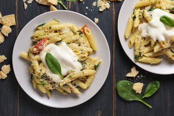 Two portions of pasta with tomatoes, spinach, parmesan and bolognese sauce. Dish in a plate on a wooden table. Top view.