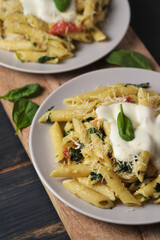 Two portions of pasta with tomatoes, spinach, parmesan and bolognese sauce on a large kitchen wooden board. Dish in a plate on a wooden table.