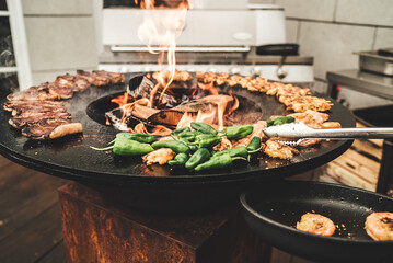 Round barbecue grill with open fire inside. Preparing meat pieces, shrimps and green peppers....