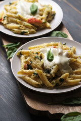 Two portions of pasta with tomatoes, spinach, parmesan and bolognese sauce on a large kitchen wooden board. Dish in a plate on a wooden table.