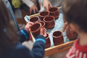 Children's hands picking up earthenware bowls with water in the Waldorf school cast.