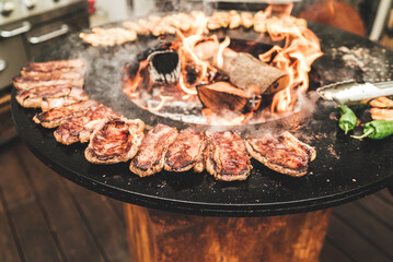Round barbecue grill with open fire inside. Preparing steaks, shrimps and green peppers. Party, BBQ, cooking and restaurant concept.
