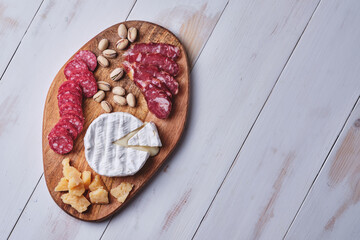 Cheese and sausage delicacies, nuts on a wooden board on an old white table. View from above.