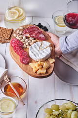 Girl prepares a romantic dinner for two. Cheese and sausage delicacies, nuts, fruits, olives, bread, grapes, wine and honey on an old white wooden table.