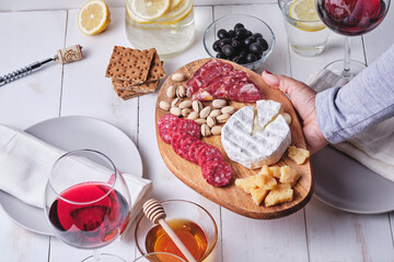 Girl prepares a romantic dinner for two. Cheese and sausage delicacies, nuts, fruits, olives, bread, grapes, wine and honey on an old white wooden table.