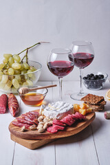 A romantic dinner for two. Cheese and sausage delicacies, nuts, fruits, olives, bread, grapes, wine and honey on an old white wooden table.