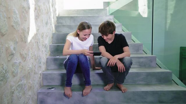 MS Boy (14-15) and girl (12-13) sitting on stairs and using smart phone 
