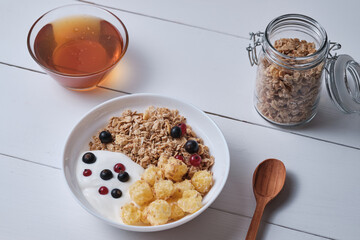 Muesli with yogurt and fresh berries in a plate. Breakfast on a white wooden table.