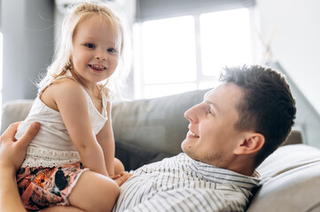 Obraz premium Father's day. Handsome happy dad spend time with his beloved adorable little daughter at home, they hugging on a couch