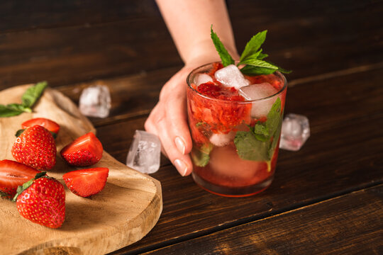 Woman's hand placing a glass with cold and refreshing strawberry summer cocktail