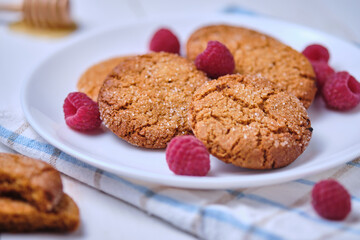 Oatmeal cookies with honey decorated with raspberries. Dessert on a towel, on a white kitchen table close-up.