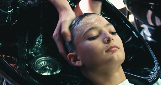 Barber washing head of the young boy in a salon in the big black sink