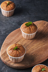 Lemon muffins with poppy seeds, decorated with mint, on a wooden board.
