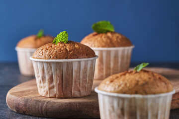 Lemon muffins with poppy seeds, decorated with mint, on a wooden board. Background color classic blue.
