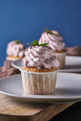 Festive cupcakes with pink cream on a plate. The dessert is decorated with mint leaves and chocolate chips. Background color classic blue.